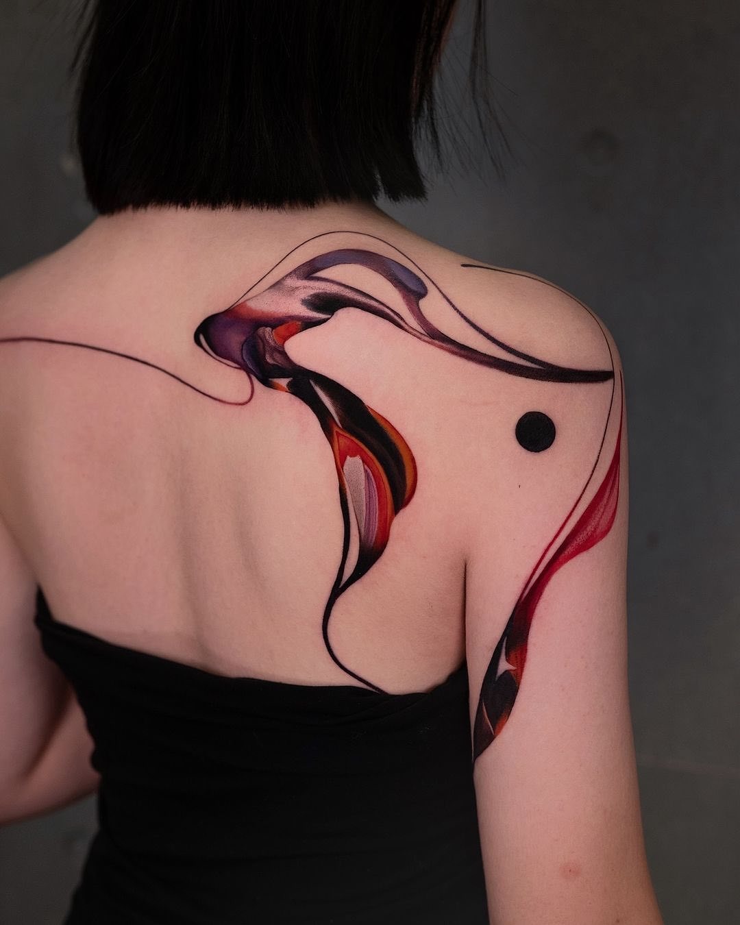 This abstract tattoo features swirling lines and colors that flow elegantly across the shoulder and back.