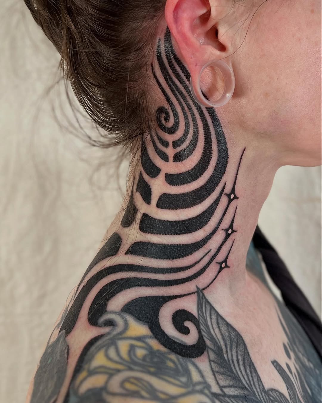 This abstract tattoo features swirling black lines gracefully wrapping around the neck.