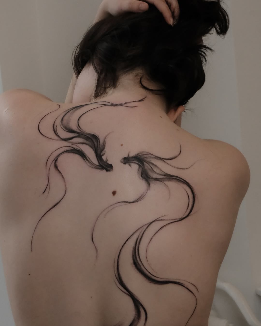 This tattoo features elegant, flowing lines that create a sense of movement across the back.