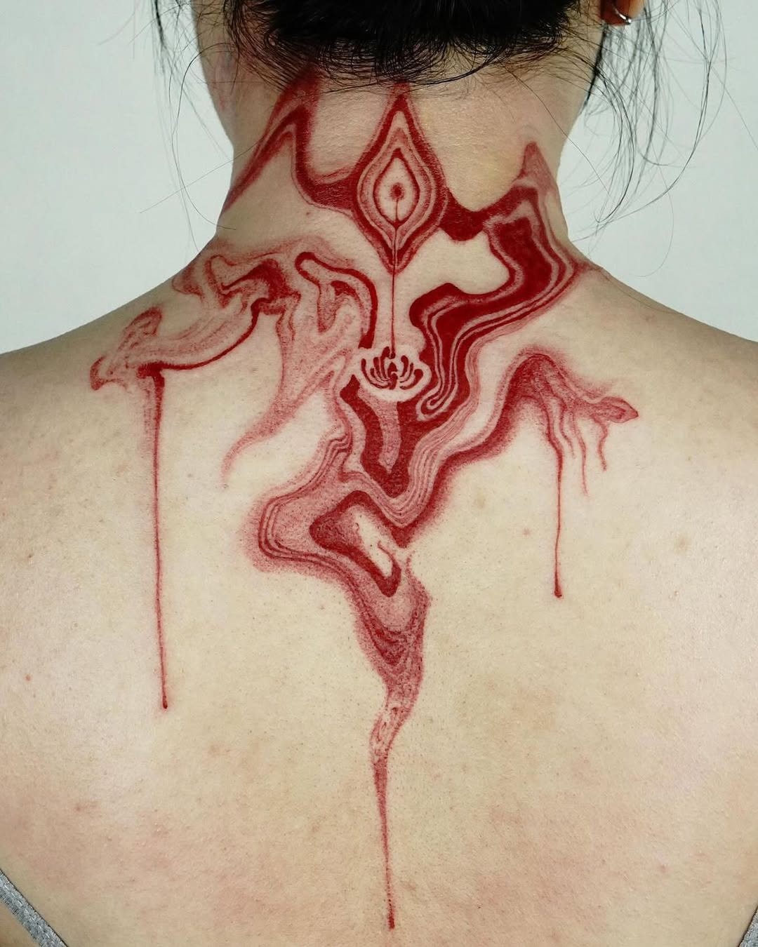 This abstract tattoo captivates with its flowing red lines, reminiscent of ink or paint gently dripping down the skin.