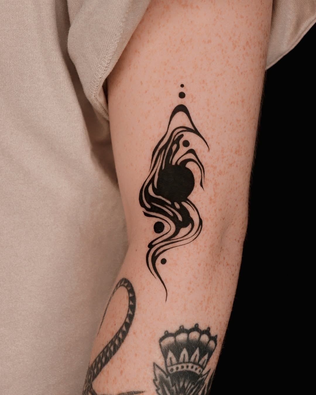 This tattoo features an abstract design of swirling lines and shapes in solid black ink, creating a striking focal point on the arm.