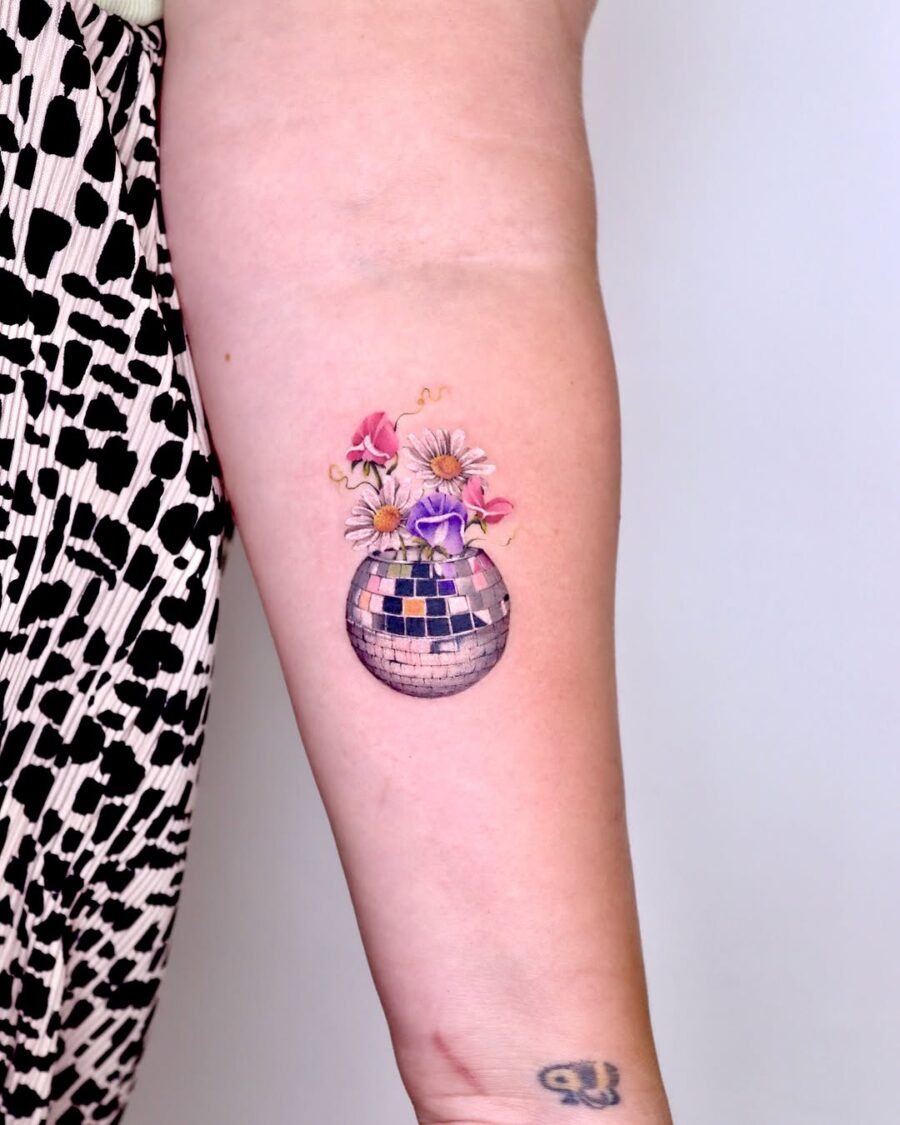 This aesthetic tattoo features a disco ball adorned with flowers, combining a sense of celebration with natural beauty.