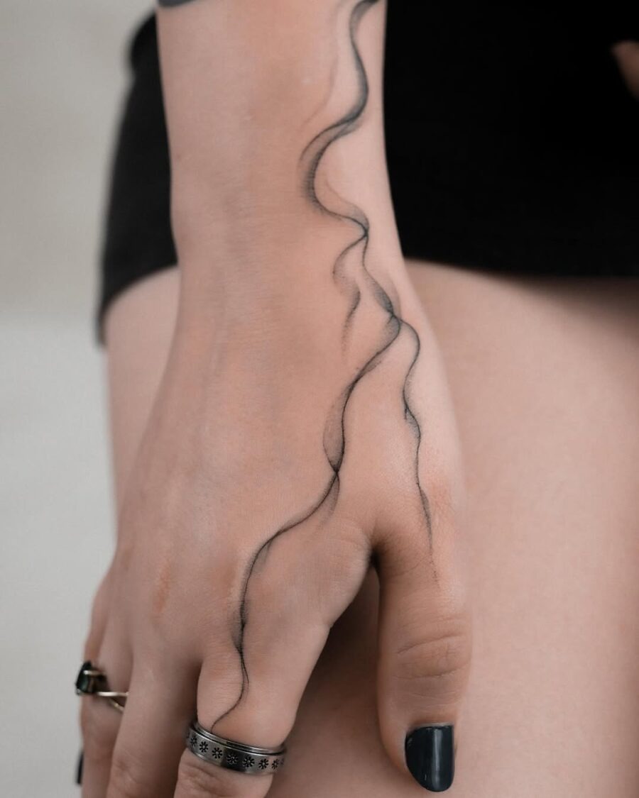 This minimalist tattoo features a flowing wave design along the hand, showing an elegant and artistic vibe.