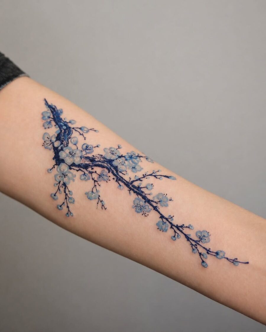 This tattoo showcases a delicate branch adorned with soft blue flowers.