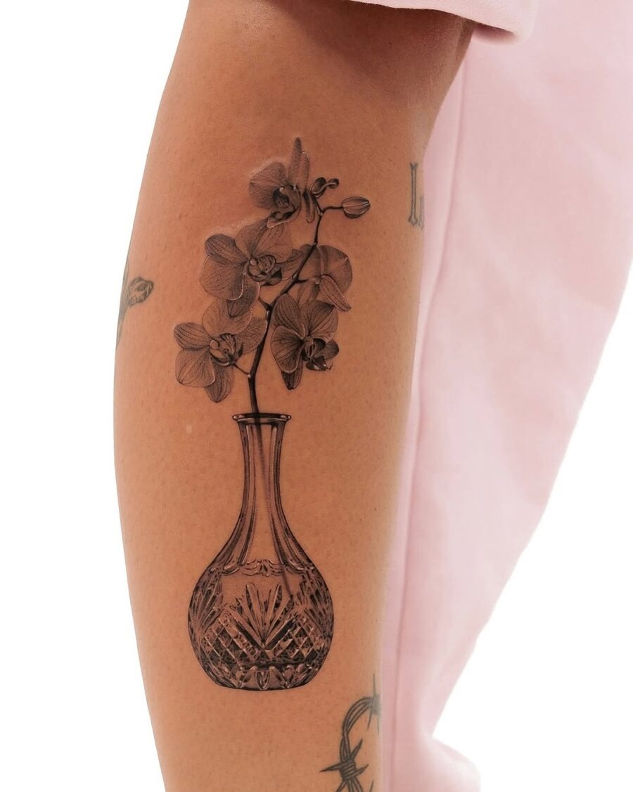 This tattoo features a beautifully designed vase with orchids, rendered in fine black ink.