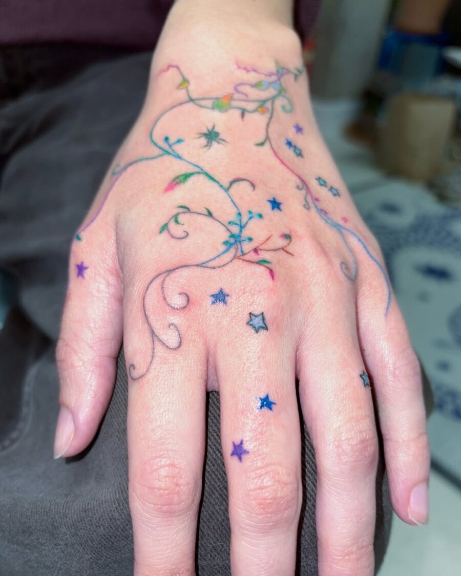 This tattoo features intricate, whimsical designs of colorful stars flowing elegantly across the hand.