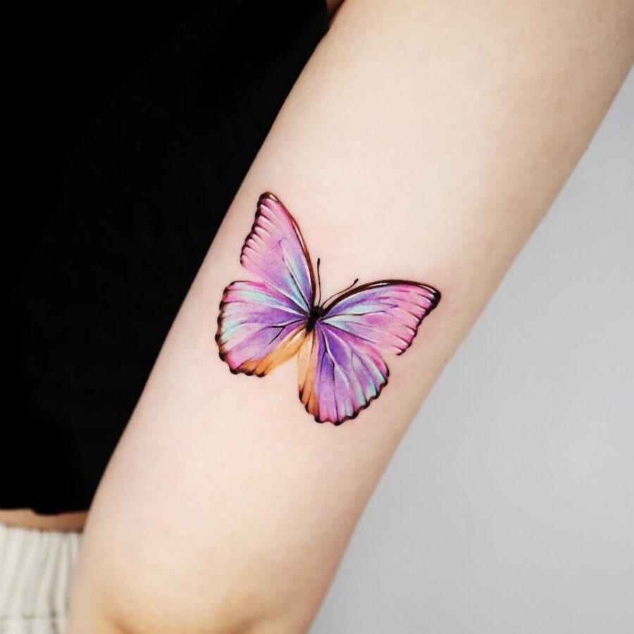 This tattoo showcases a beautifully detailed butterfly with pinks and purples.