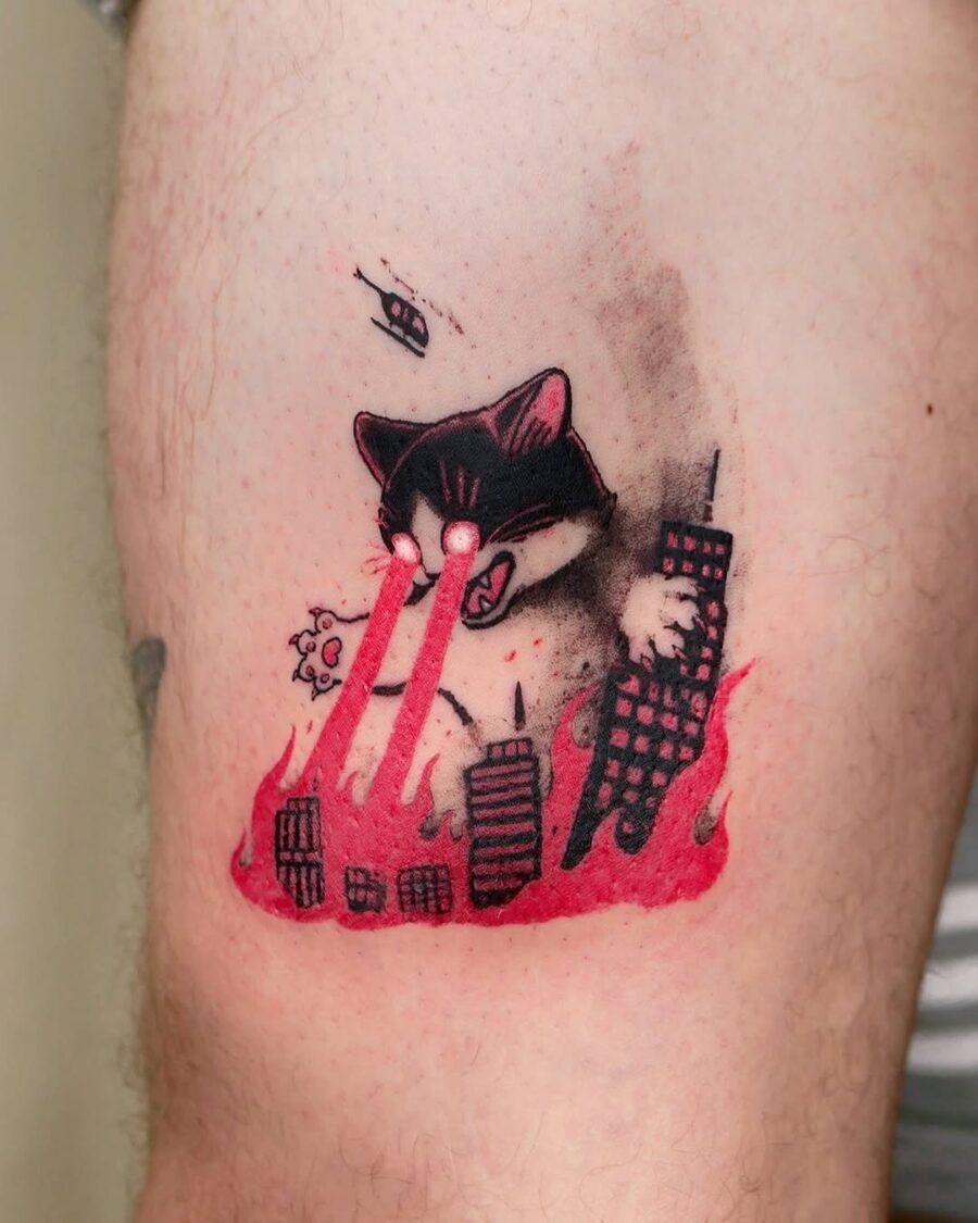 This tattoo features an imaginative cat with laser beams shooting from its eyes, creating a comical scene of destruction in a cityscape.
