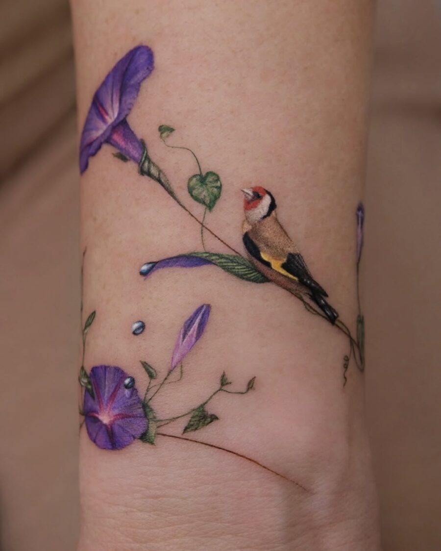 This tattoo features a beautifully detailed bird perched among purple flowers.