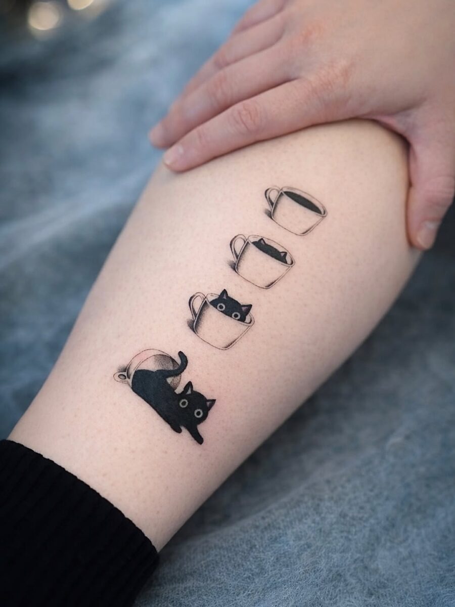 This tattoo features playful black cats emerging from coffee cups.