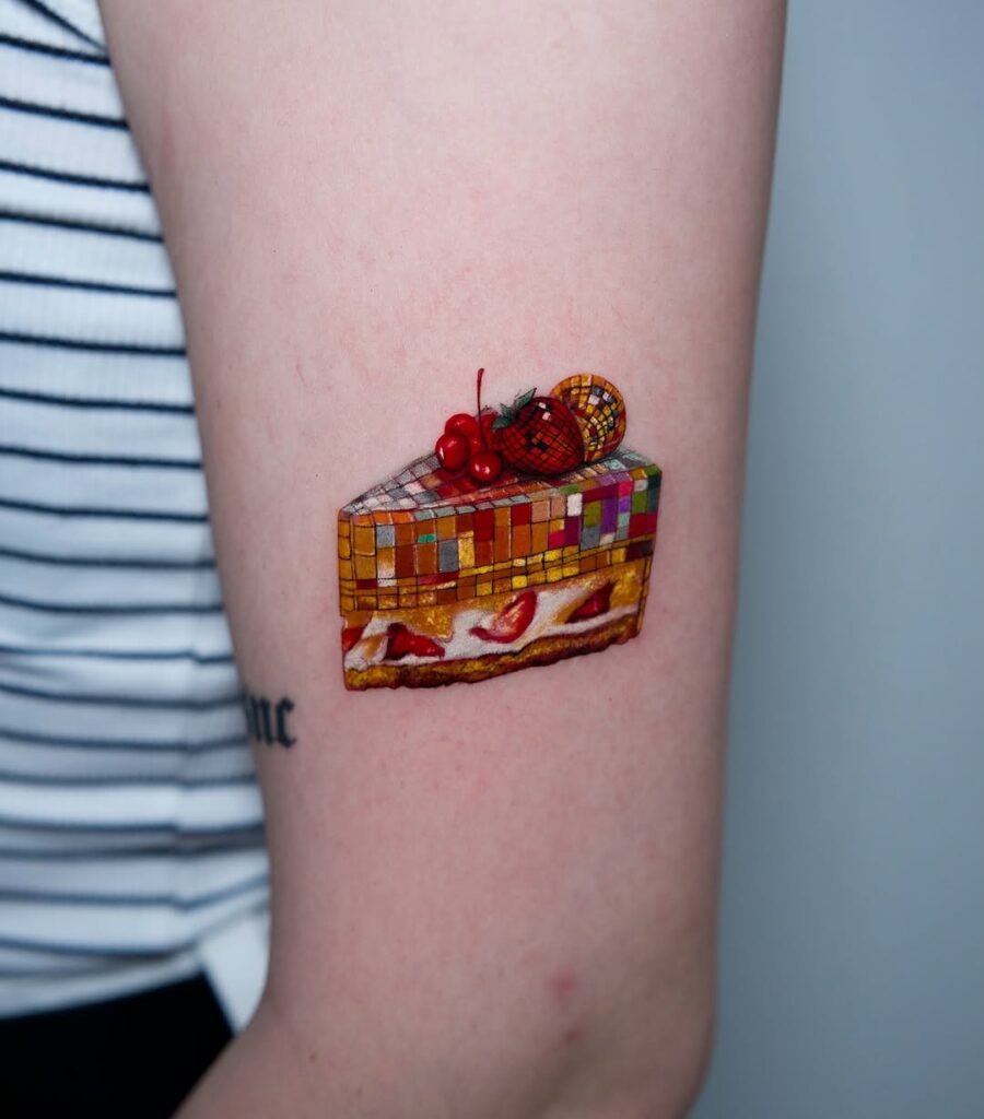 This tattoo showcases a beautifully detailed slice of cake, bursting with colors and playful elements.