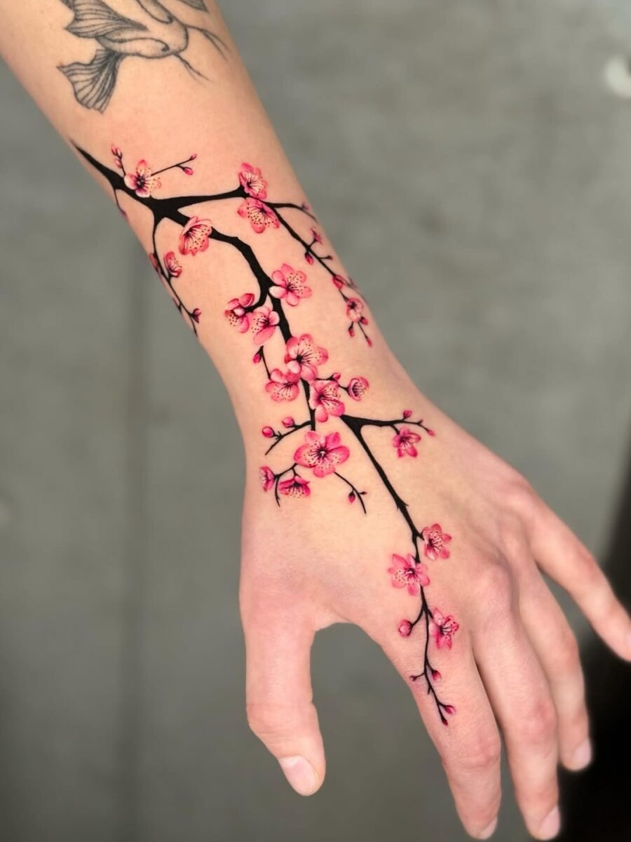 This tattoo features a delicate cherry blossom branch winding elegantly around the wrist.