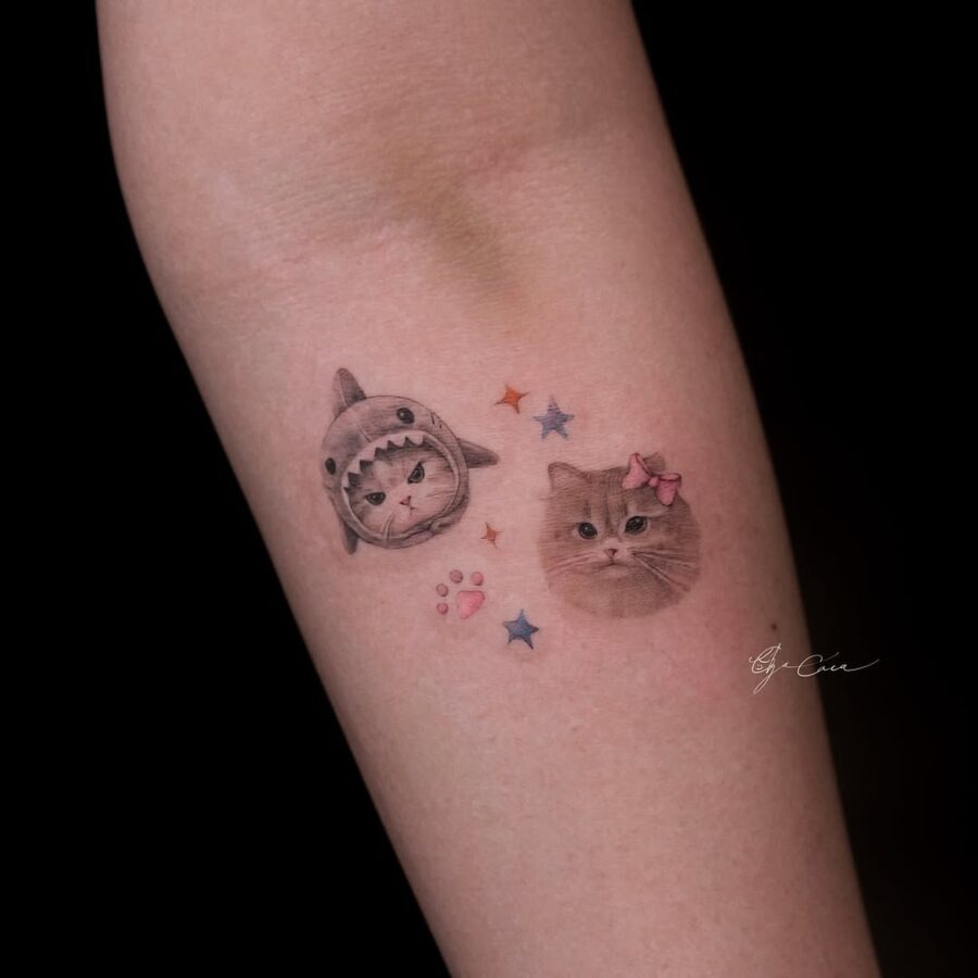 This tattoo features an adorable shark wearing a cat-themed hat alongside a charming cat with a bow.