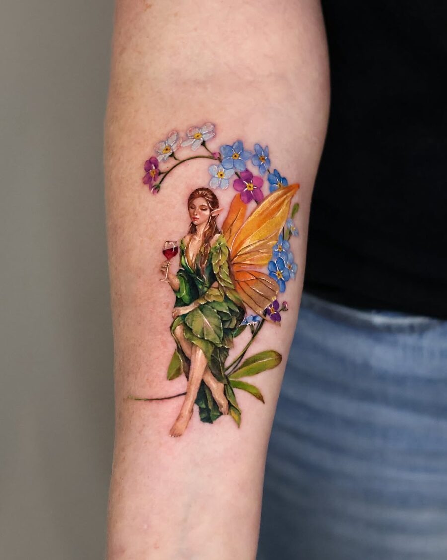 This tattoo showcases a beautifully crafted fairy, draped in lush green leaves and surrounded by flowers.