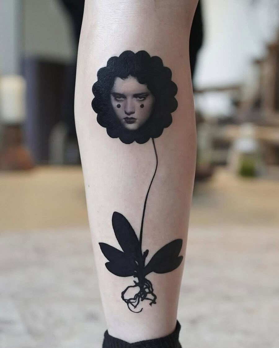 This tattoo features a striking design of a face framed by a floral silhouette, blending realism with abstract elements.