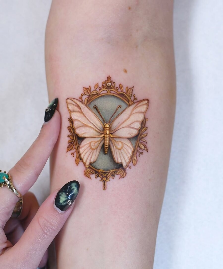 This tattoo showcases a beautifully detailed butterfly surrounded by an ornate frame.