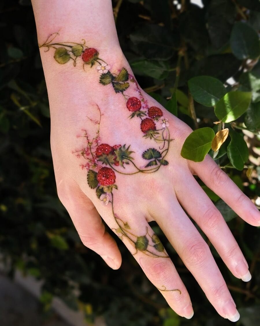 This stunning hand tattoo features beautiful strawberries intertwined with delicate vines and flowers.