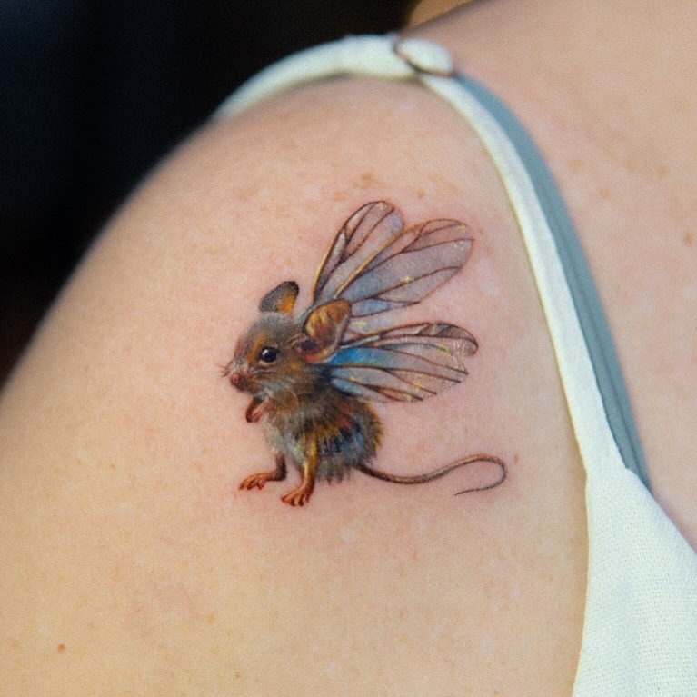 This adorable tattoo features a tiny mouse with delicate fairy wings, bringing a playful charm to the skin.
