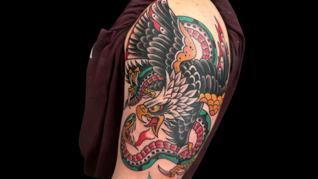 Traditional eagle fighting snake tattoo with sharp claws and bared serpent fangs on forearm