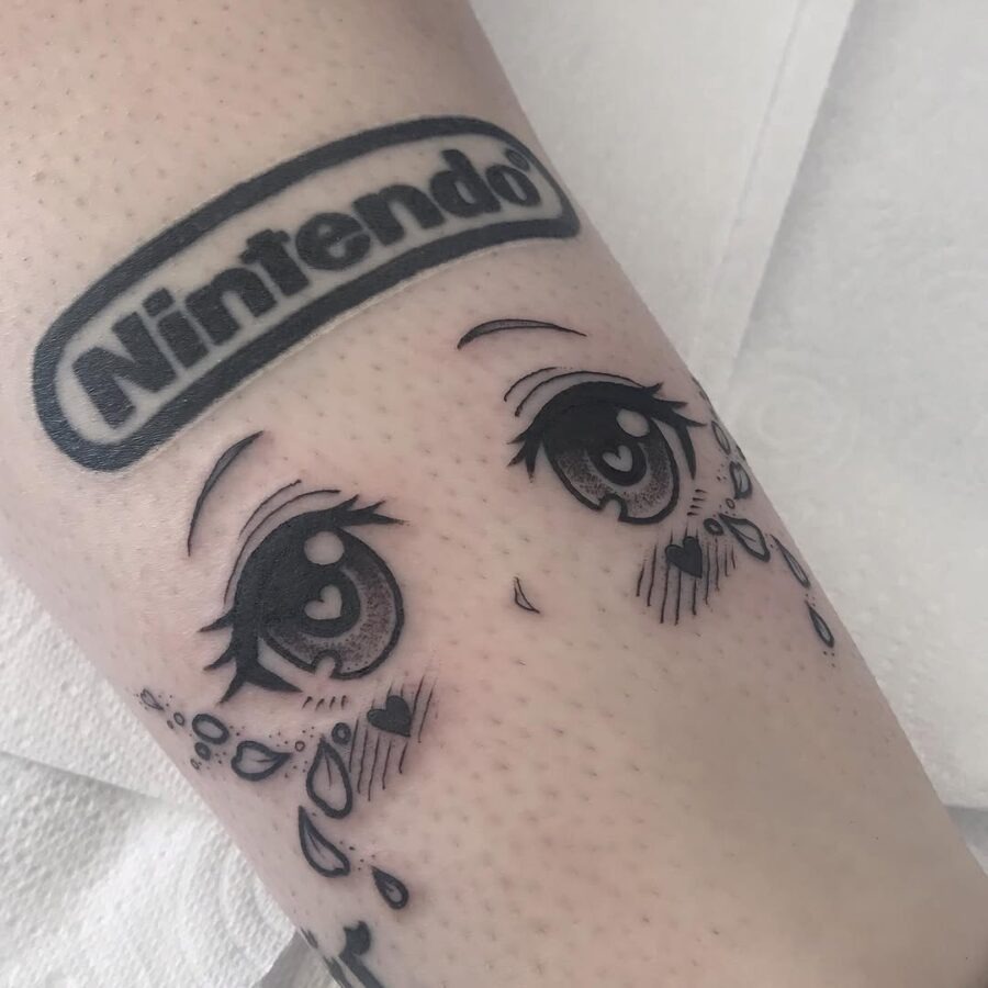 This tattoo features beautifully detailed anime eyes with a playful Nintendo logo above.