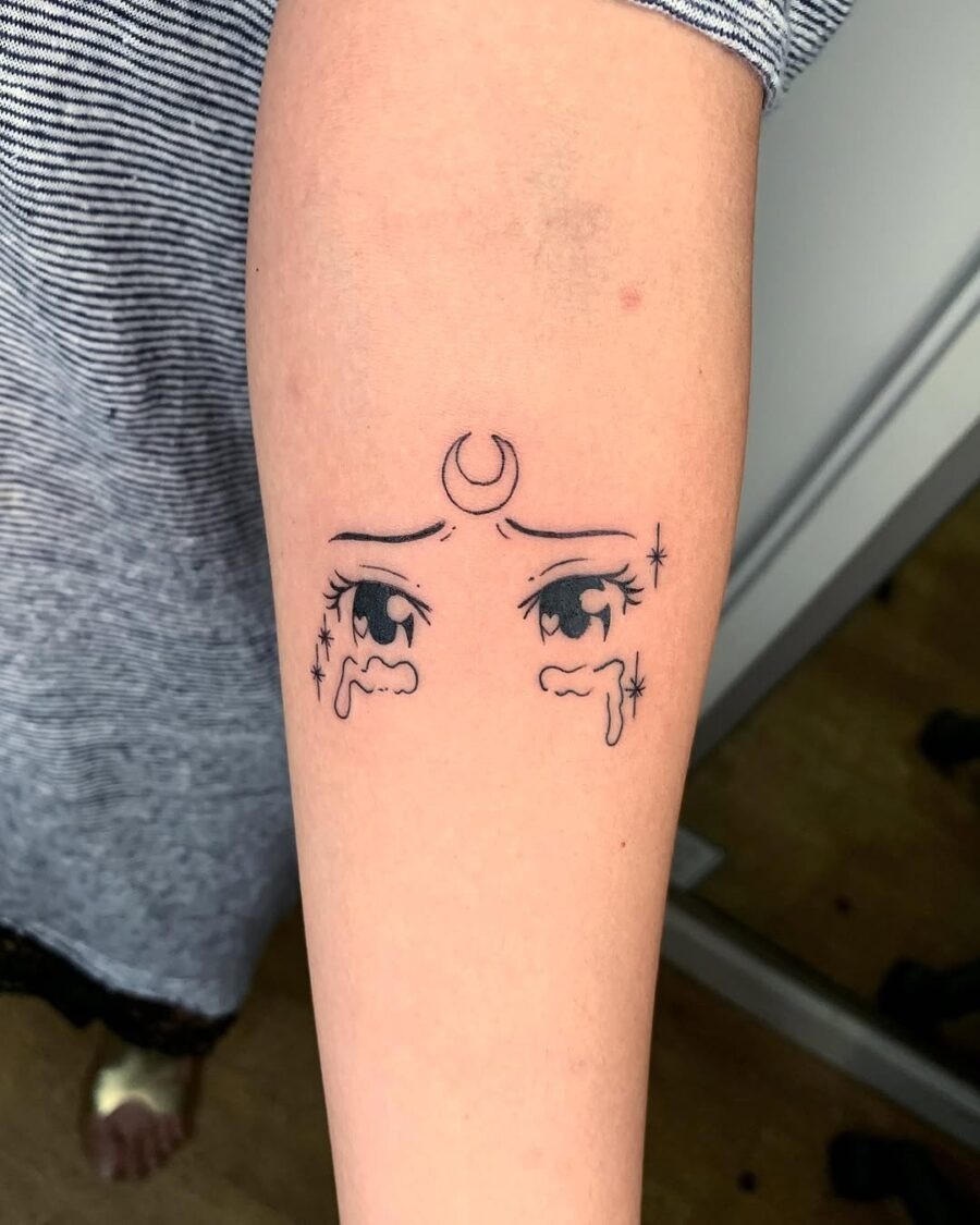 This tattoo features expressive anime eyes adorned with a crescent moon and stars.