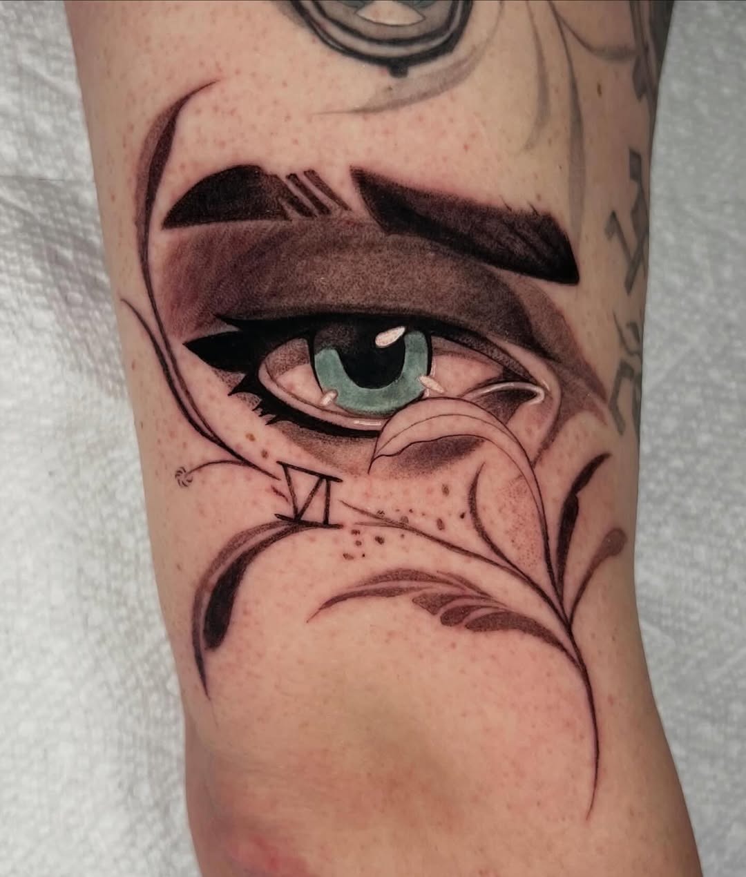 This tattoo showcases a striking anime-style eye, complemented by delicate foliage.