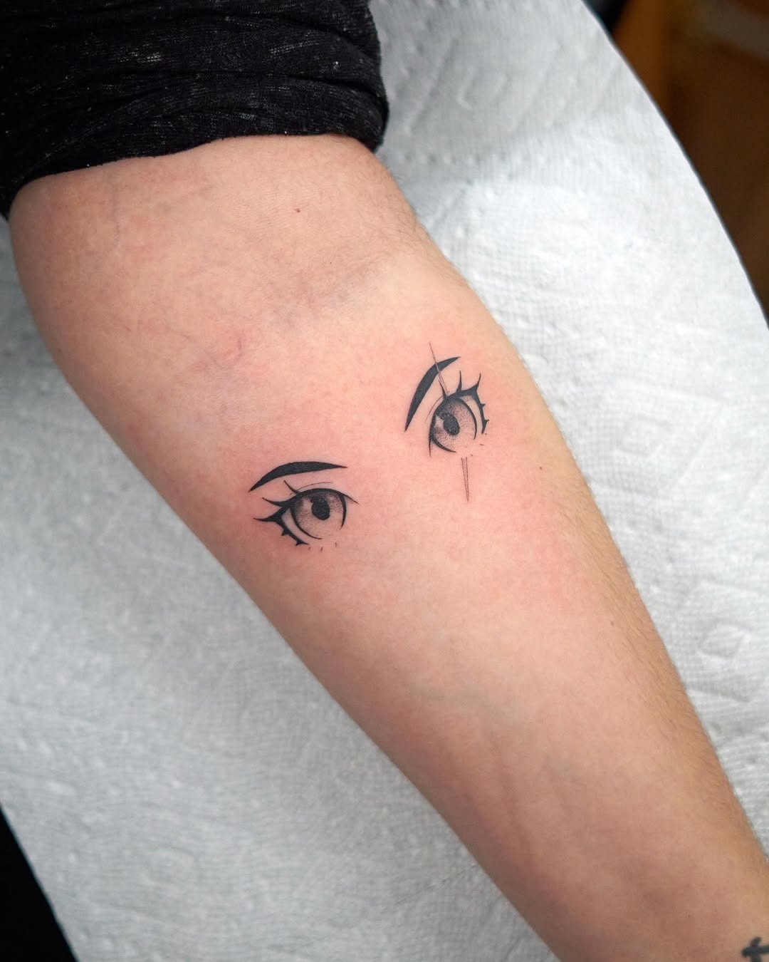 This tattoo showcases a pair of striking anime eyes done in minimalist black ink.