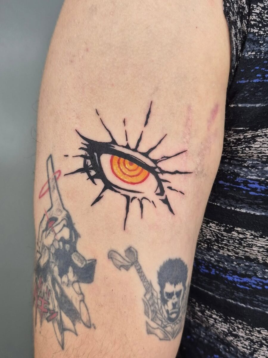 This tattoo showcases a dramatic anime eye, featuring an intense orange iris and unique black spiky accents.