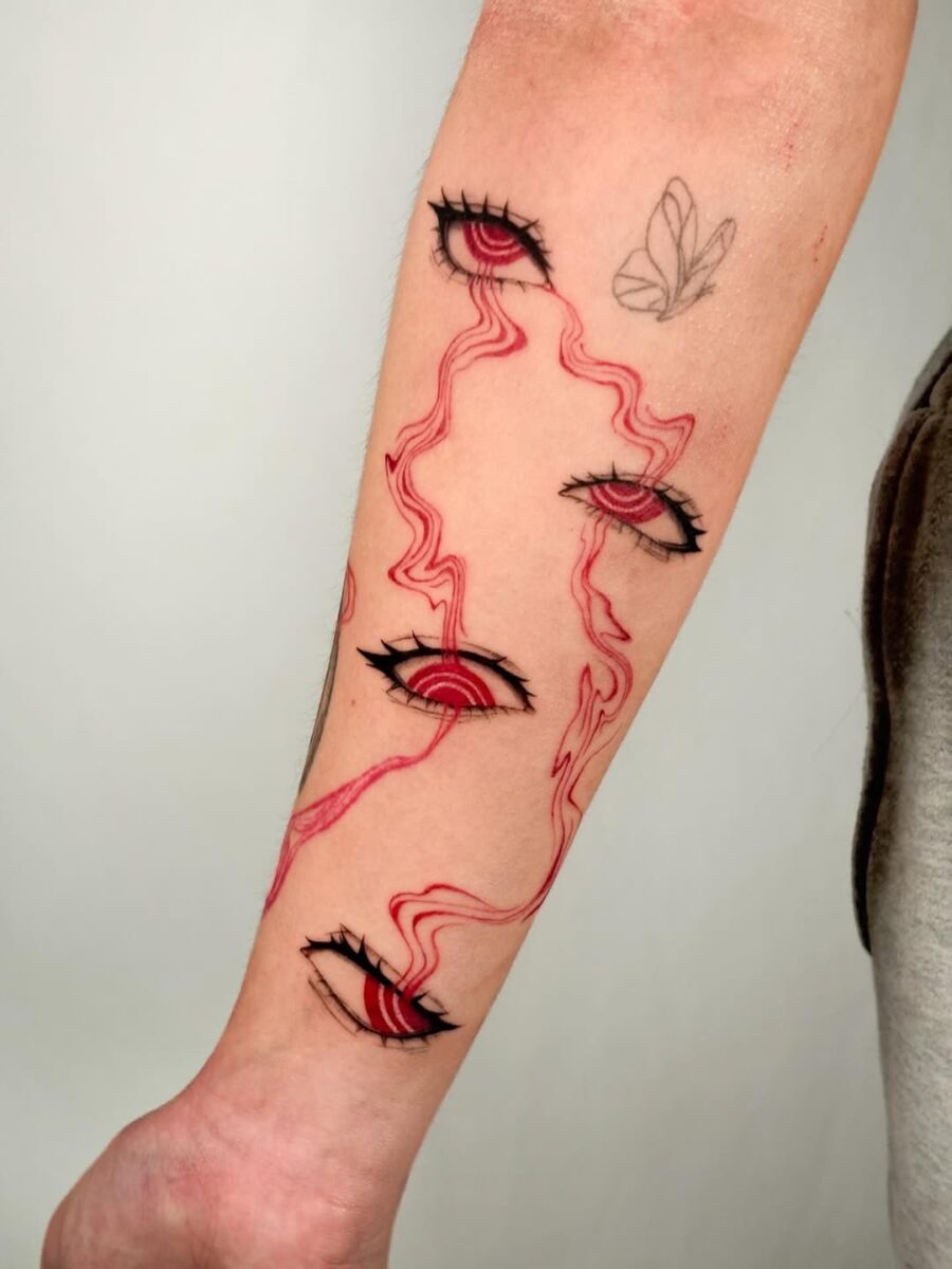 This tattoo features a bold arrangement of anime-style eyes, intertwined with striking red lines creating a dynamic effect.