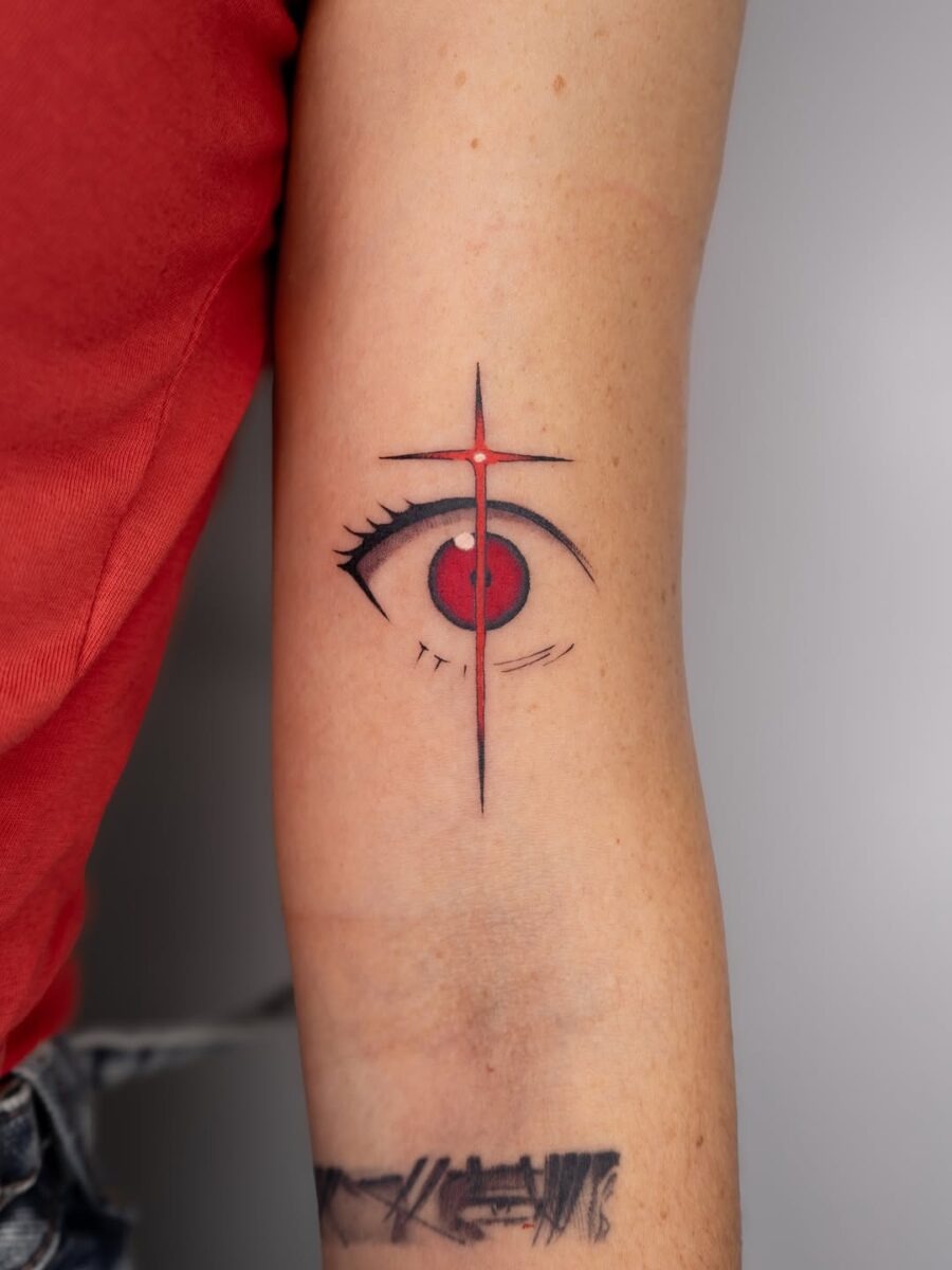 This tattoo features a captivating red eye at its center, highlighted by bold black lines and a vertical cross.