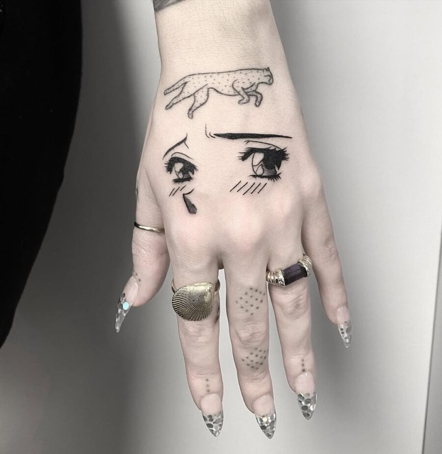 This tattoo features striking anime eyes adorned with a tear, elegantly placed on the hand.