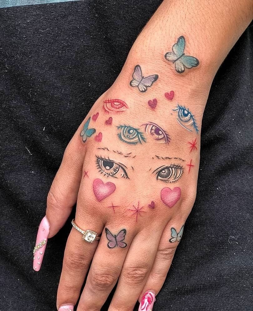 This tattoo showcases a playful array of anime eyes, butterflies, and hearts on the hand.