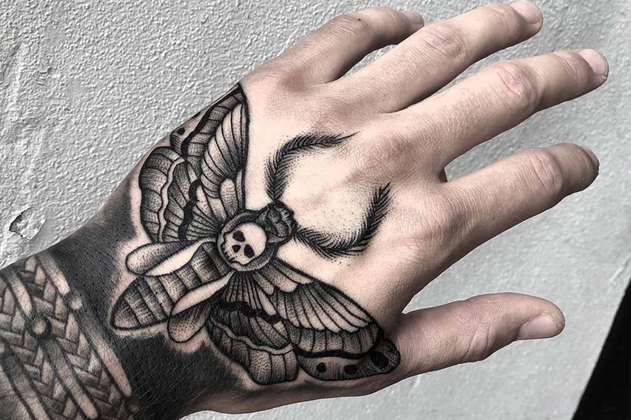 The death's-head moth tattoo on the hand is a bold choice for those who appreciate a blend of dark symbolism and intricate design.