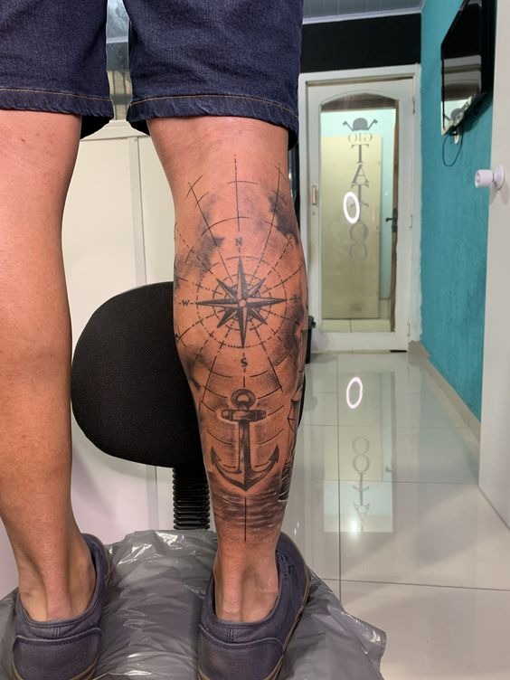 This leg tattoo features a striking combination of a compass and an anchor, two symbols deeply rooted in nautical themes.