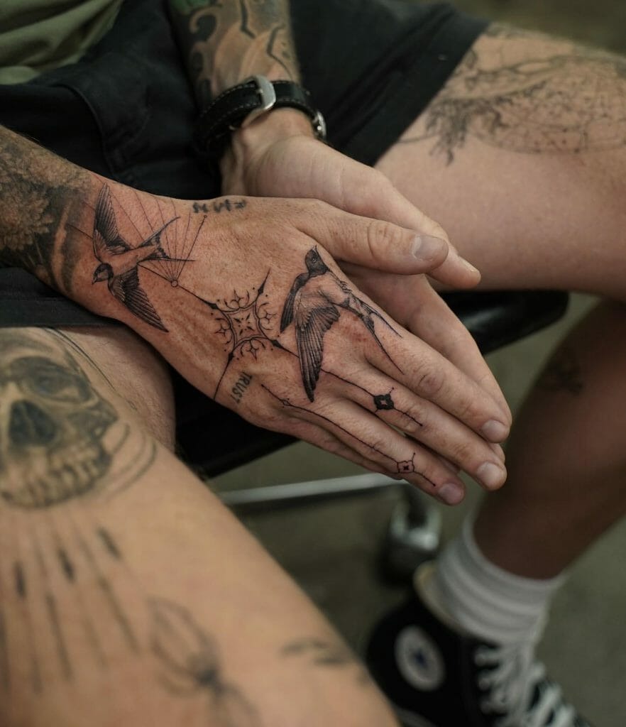 Combining the imagery of swallows and a compass, this hand tattoo is a symbolic piece that represents direction, freedom, and guidance.