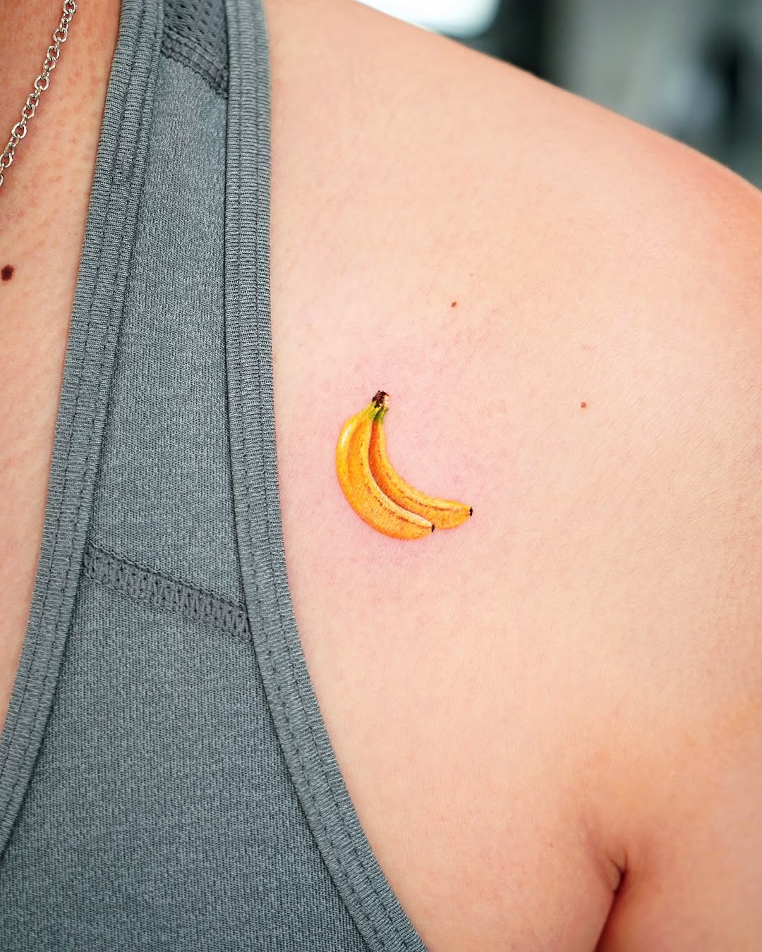 This tattoo showcases two yellow bananas, nestled on the wearer's upper arm.