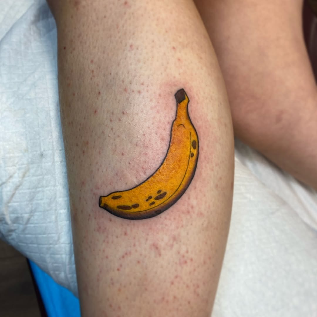 This banana tattoo features a playful design, showing a bright yellow color with detailed shading.