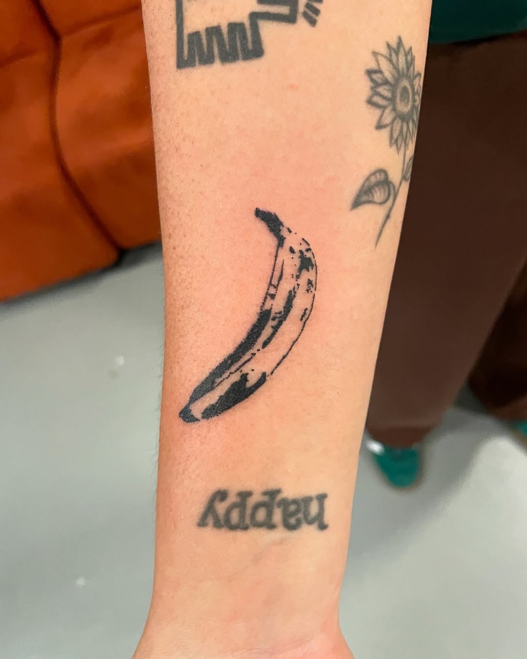 This banana tattoo features a simple, black-ink design on the forearm.