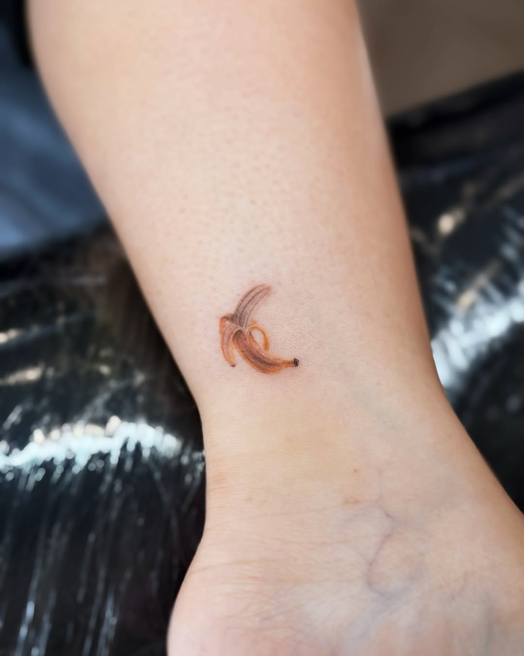 This playful banana tattoo features a minimalistic design, showing a single banana peel with soft brown lines.