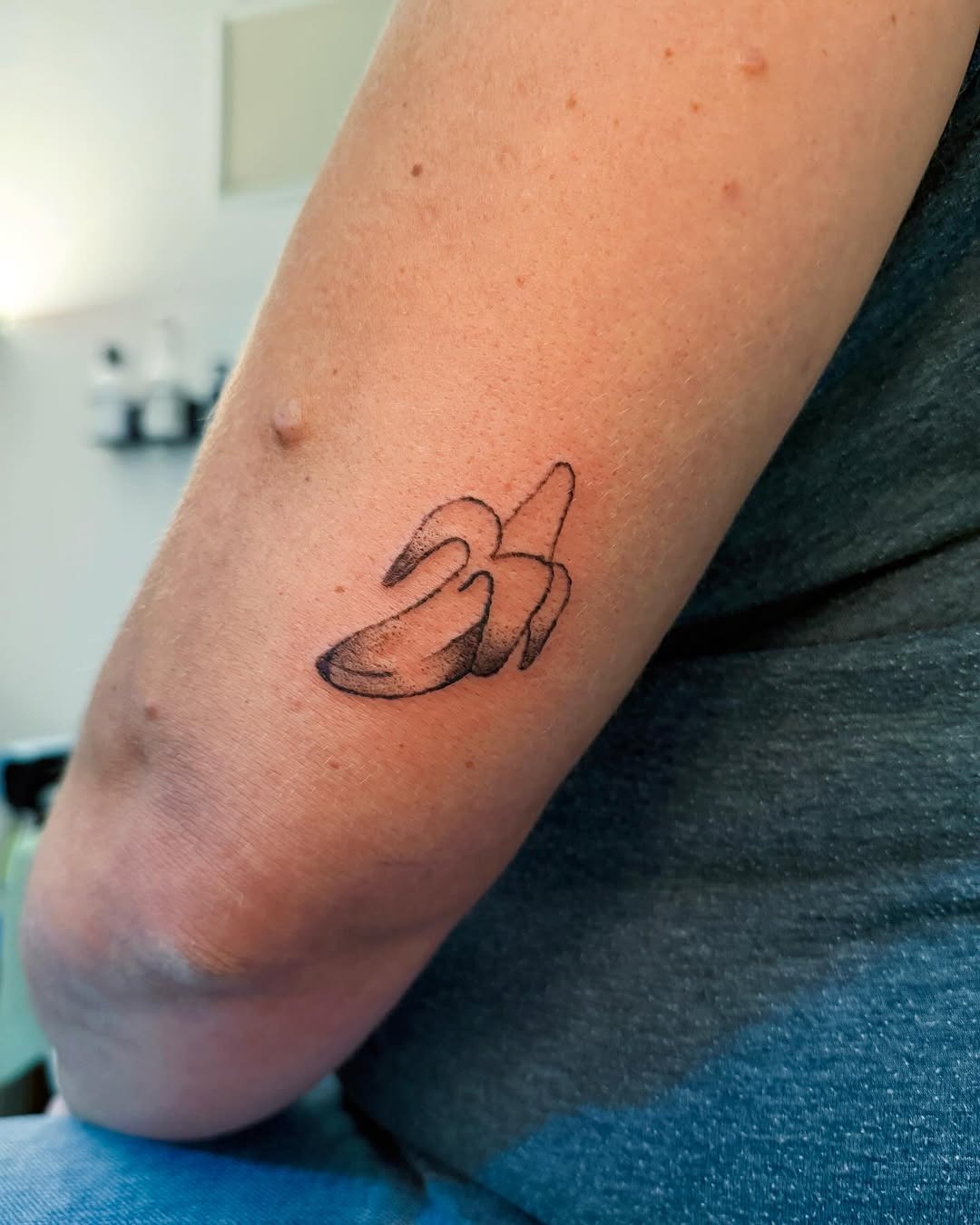 This tattoo features a minimalist design of a banana, inked on the forearm.
