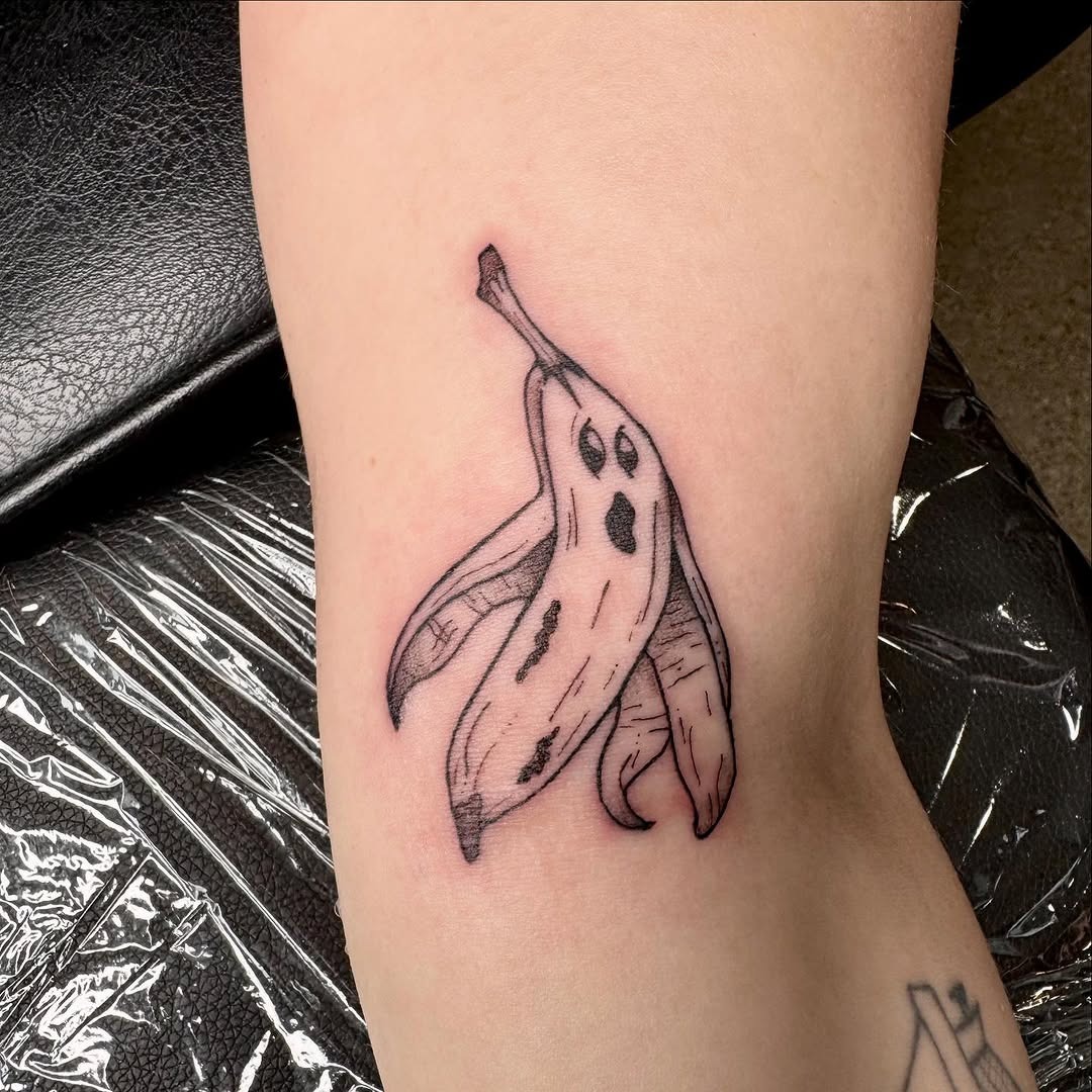 This tattoo features a whimsical banana with adorable ghost-like faces.