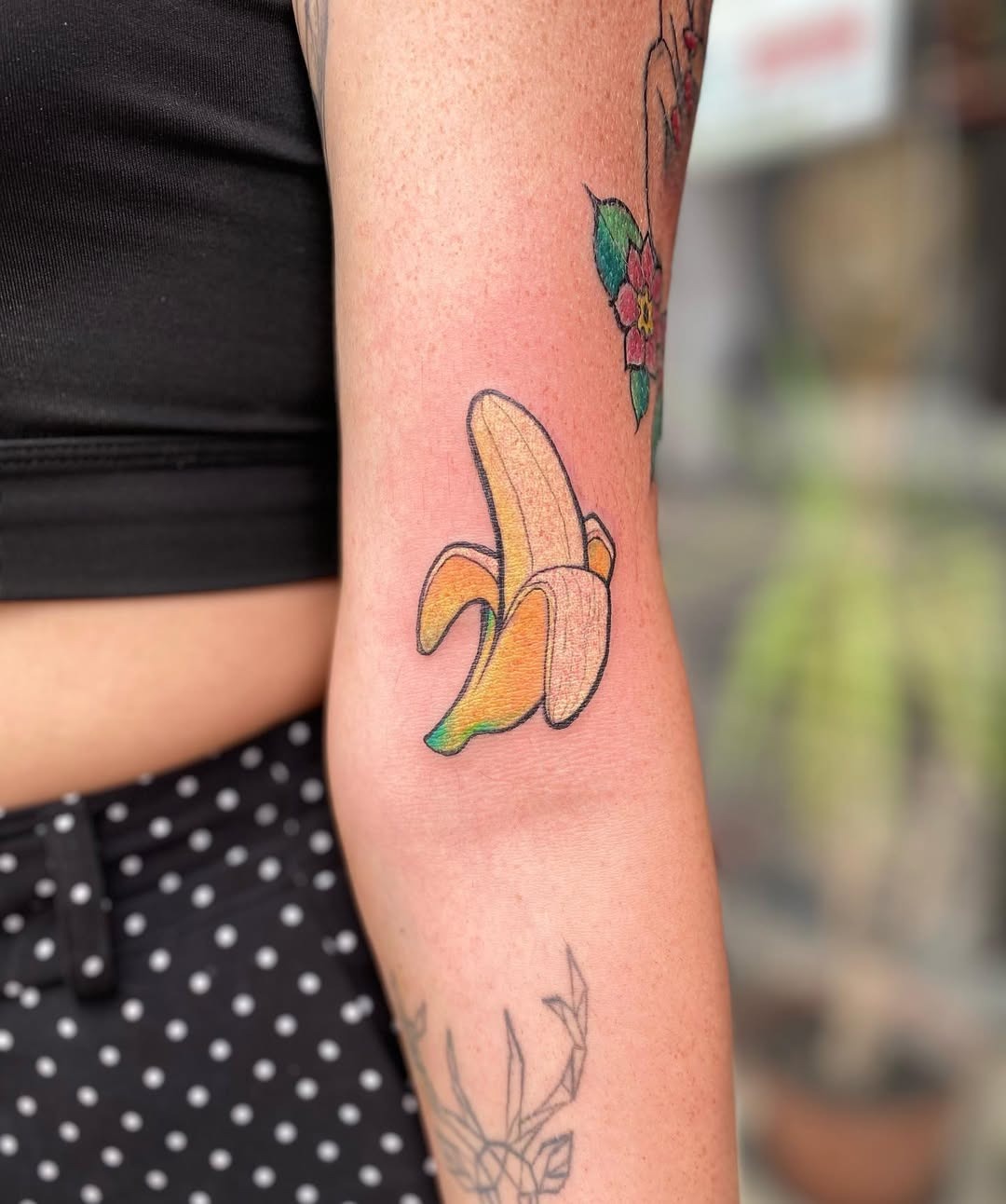 This tattoo showcases a bright and playful banana resting on the elbow.