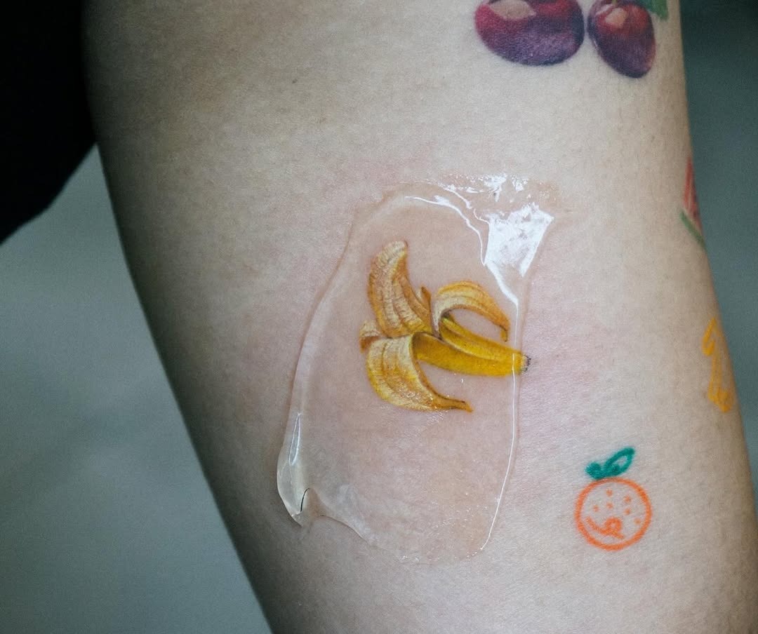 This tattoo showcases a realistic banana design encased in a glossy wax layer, adding a unique touch.