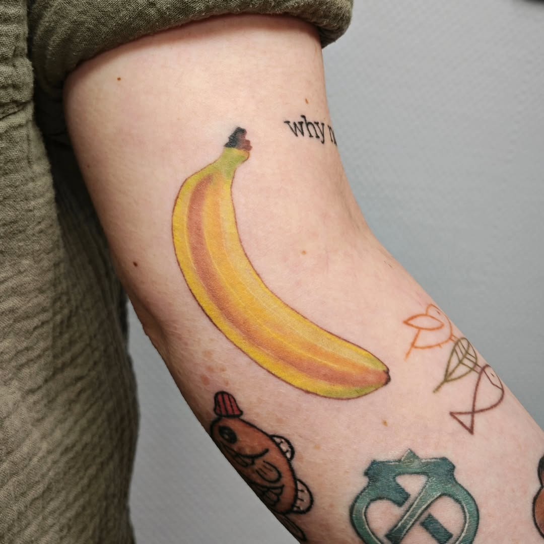 This colorful banana tattoo showcases a bright yellow banana design on an arm.