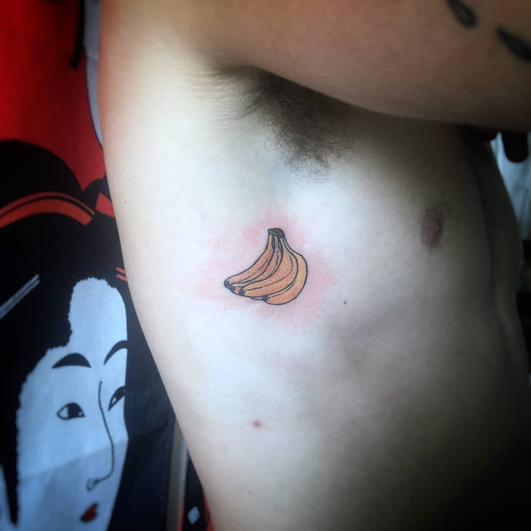 This tattoo features a playful banana design inked on the ribcage.