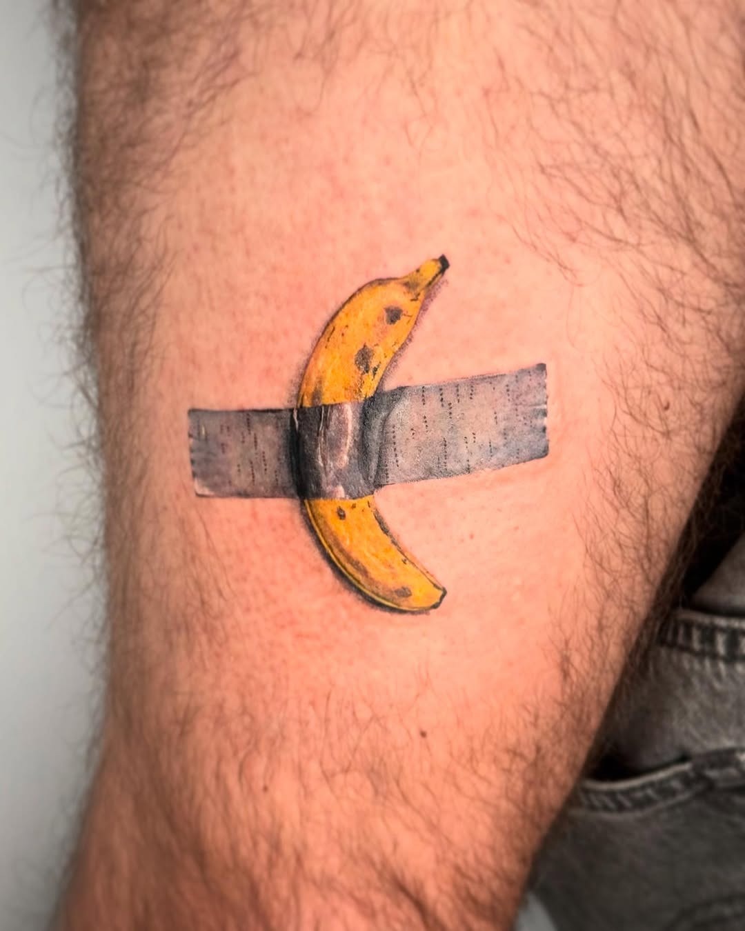 This tattoo features a realistic banana taped to the skin, creating a fun and quirky visual.