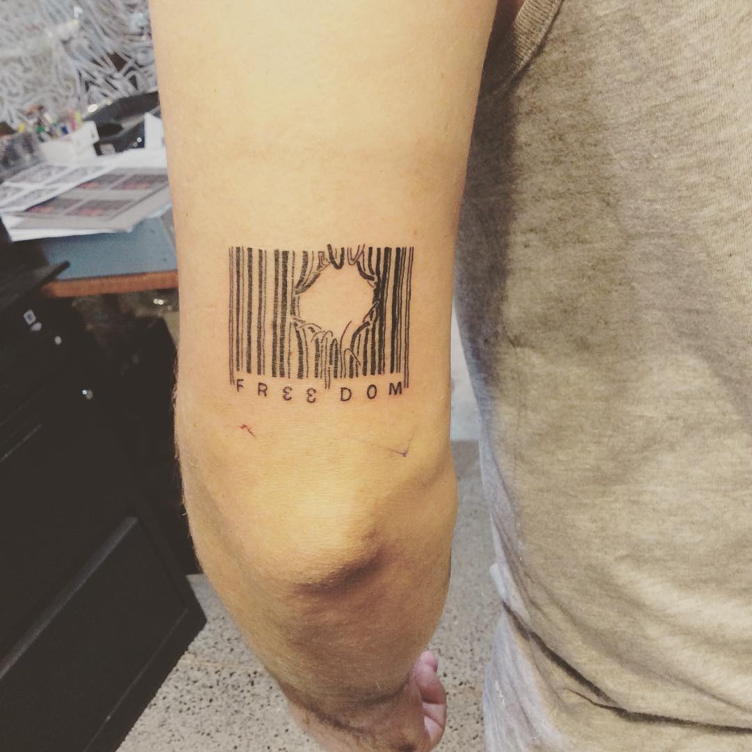 This tattoo features a striking barcode design with the word 'FREEDOM' unique incorporated into its stripes.