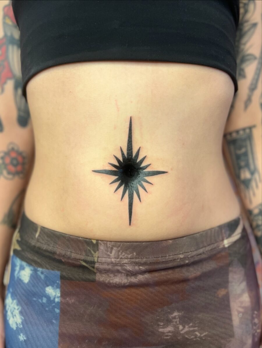 This belly tattoo features a bold, black star compass design, adding a unique flair to the midsection.