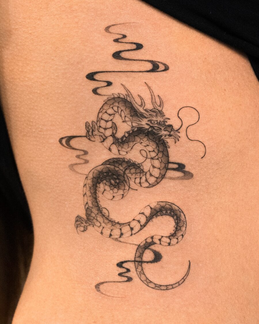 This tattoo features a beautifully detailed dragon coiling around the belly, surrounded by soft, flowing clouds.
