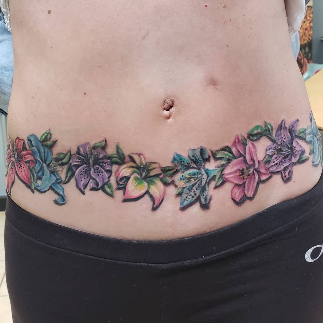 This tattoo features an array of colorful lilies wrapped around the belly.